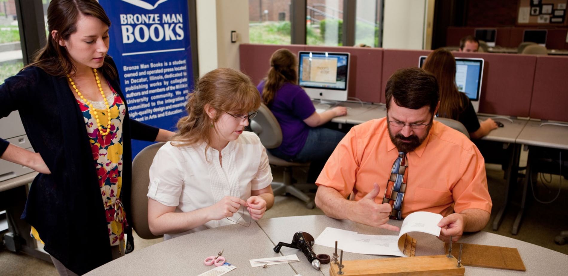 This photo shows faculty member Dr. Brooks flipping through a book with two students at a Bronze Man Books event.